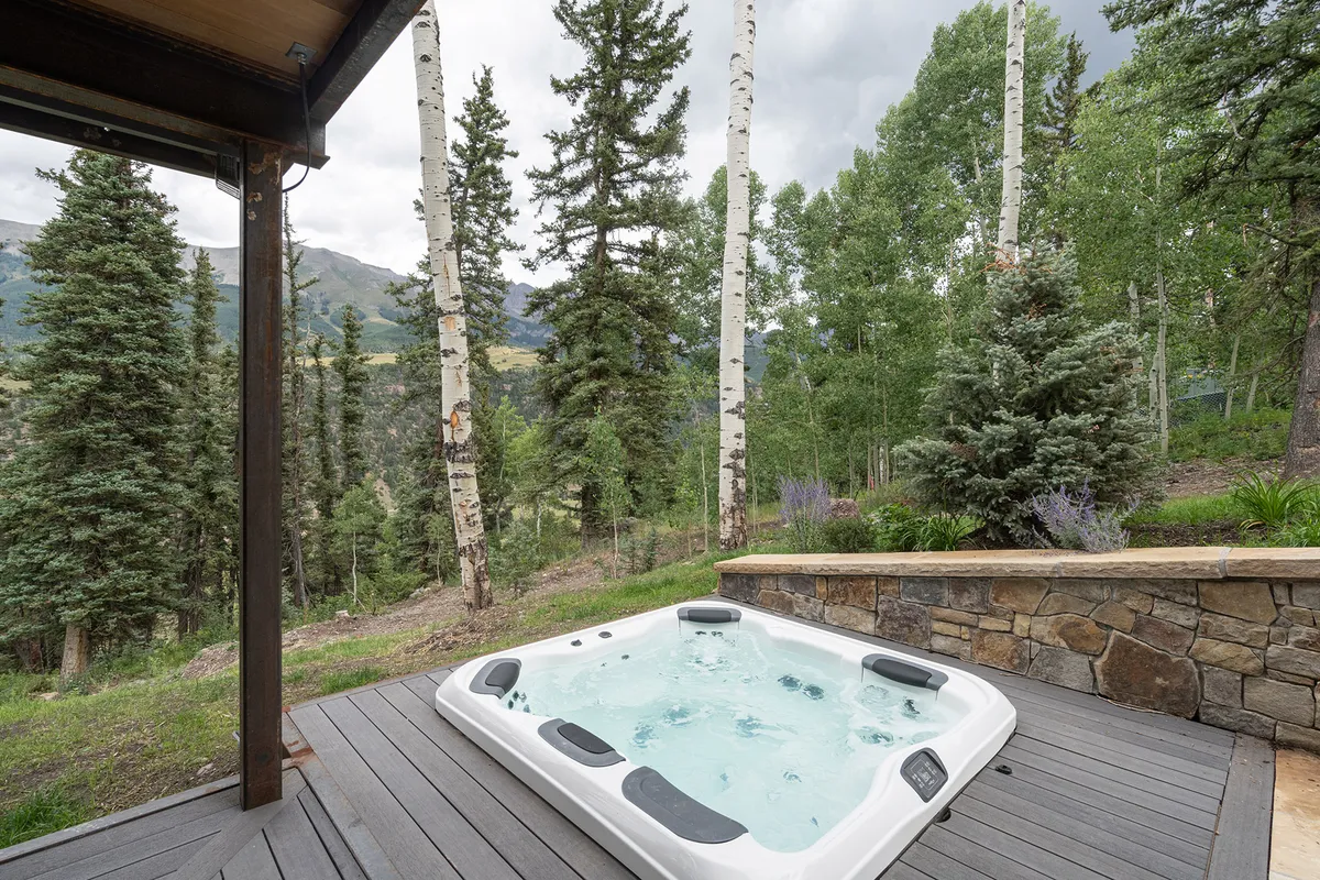 This exterior shot features a private jacuzzi set amidst trees with a majestic mountain view in the background. The scene invites relaxation and luxury, promising year-round enjoyment regardless of the season.