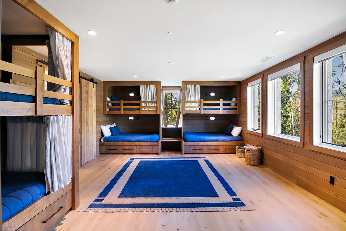 A playful, inviting bunk room with multiple bunk beds, a cozy rug, and large windows streaming in natural light. This space is designed for kids to sleep, play, and socialize in comfort.