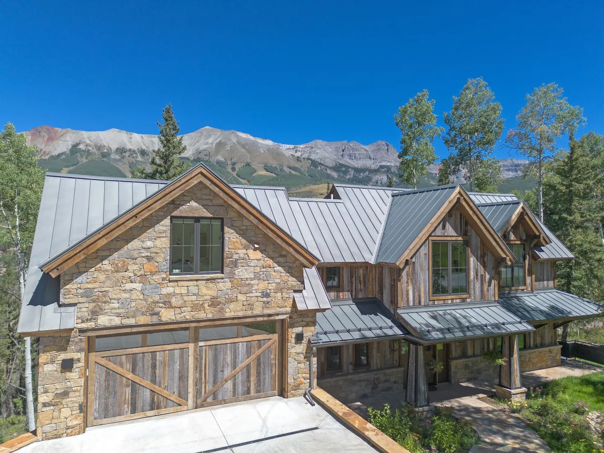 This image showcases the exterior of Cloud View, with its inviting stone facade, metal roof, large windows, and serene natural surroundings. The mountain backdrop emphasizes the property's stunning location and connection to the outdoors.