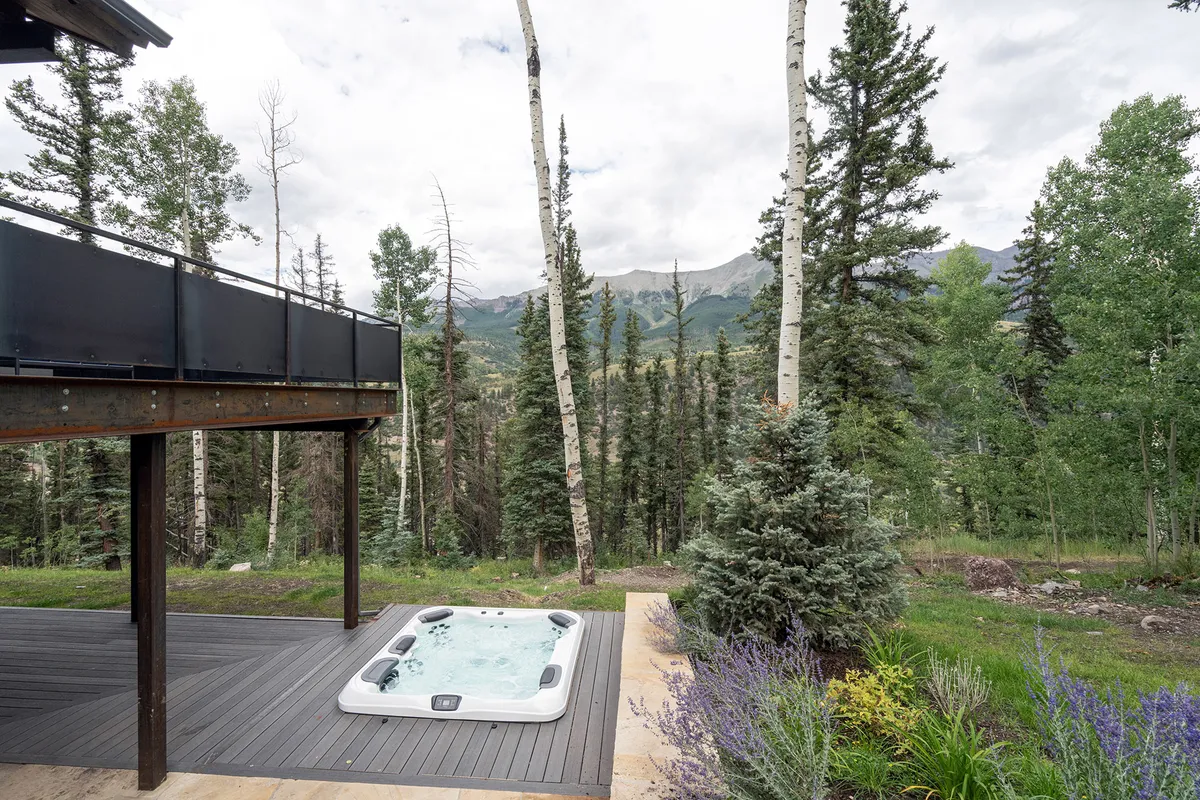 An exterior shot of the lower deck featuring a hot tub surrounded by trees and mountain views. The tranquil setting is ideal for relaxing soaks and stargazing under the Colorado sky.