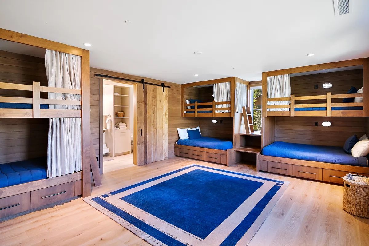This cheerful bunk room features multiple bunk beds, an area rug for play, and warm wooden accents. The layout encourages both rest and imaginative play, capturing the spirit of fun and togetherness described for the children’s space.