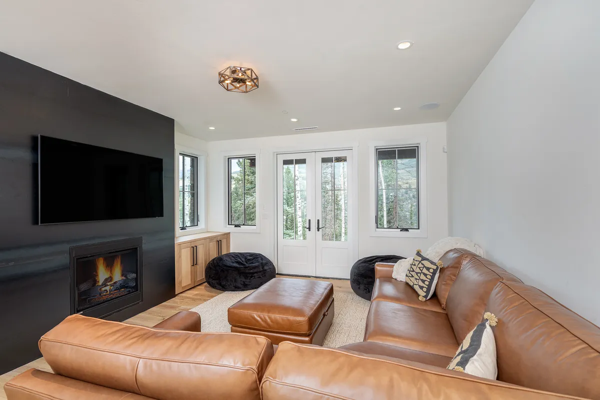 A modern, cozy media room featuring a leather sectional sofa, wall-mounted TV, and fireplace. The room also has double French doors that hint at access to the outdoors, making it perfect for movie marathons or game nights.