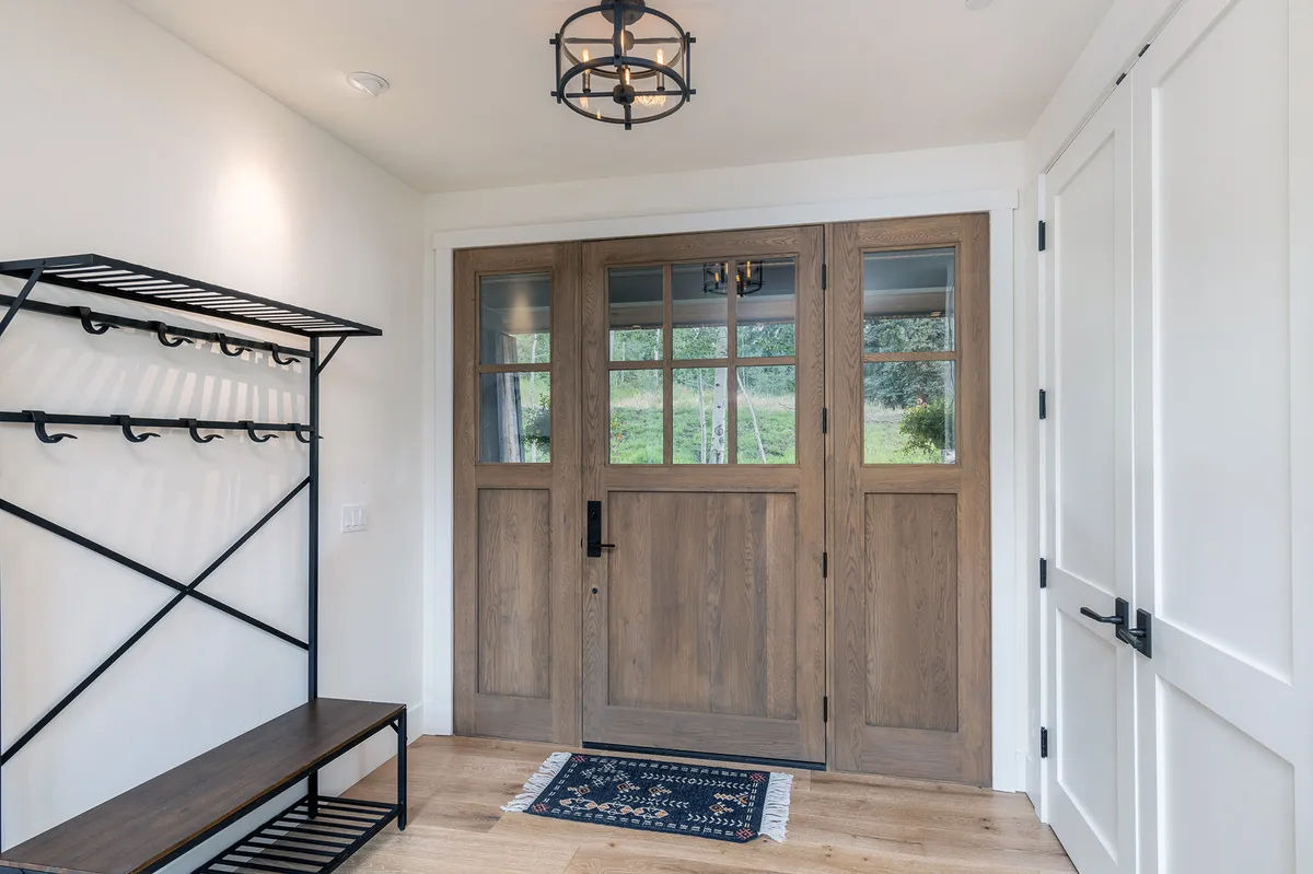 A warm and welcoming entryway featuring wooden double doors, a cozy entry rug, and a stylish lighting fixture, providing a sense of coming home and a practical area for unloading gear.