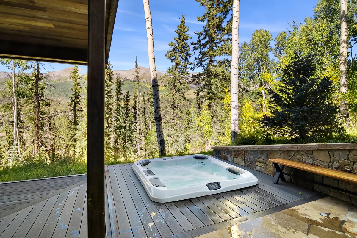 A serene, inviting hot tub on a wooden deck, surrounded by trees and offering a sweeping view of the mountains. The warm water and natural setting evoke post-adventure relaxation and immersion in nature.